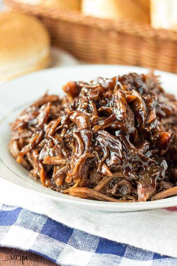 These Dump and Go Slow Cooker Recipes require no cooking or browning beforehand -- simply throw it in and walk away! Easy crock pot dump meals for busy weeknights and back to school! Chicken, beef, pork, or vegetarian -- there's something for everyone! #slowcooker #crockpot #dinner #recipes pile of honey balsamic pulled pork on white plate with basket of buns in the background