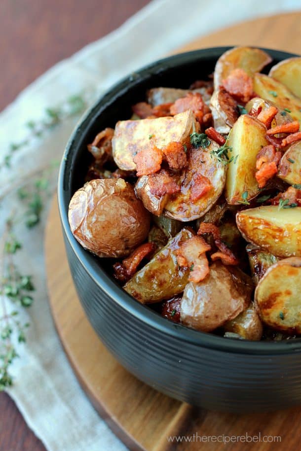 close up of warm maple bacon potato salad in black bowl on wooden cutting board