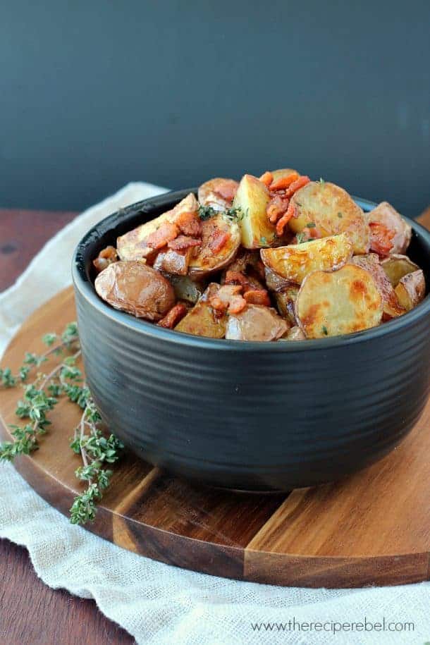 black bowl filled with maple bacon potato salad and fresh thyme on the side