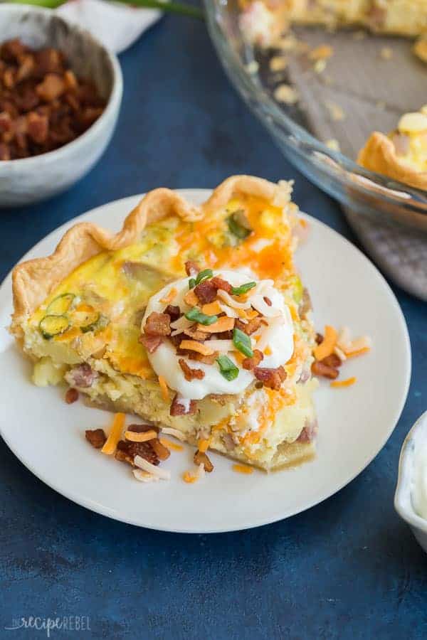 slice of loaded baked potato quiche on white plate with sour cream bacon bits cheddar cheese and green onions