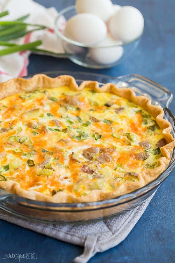 easy loaded baked potato quiche in glass pie plate on blue background with fresh eggs in the background