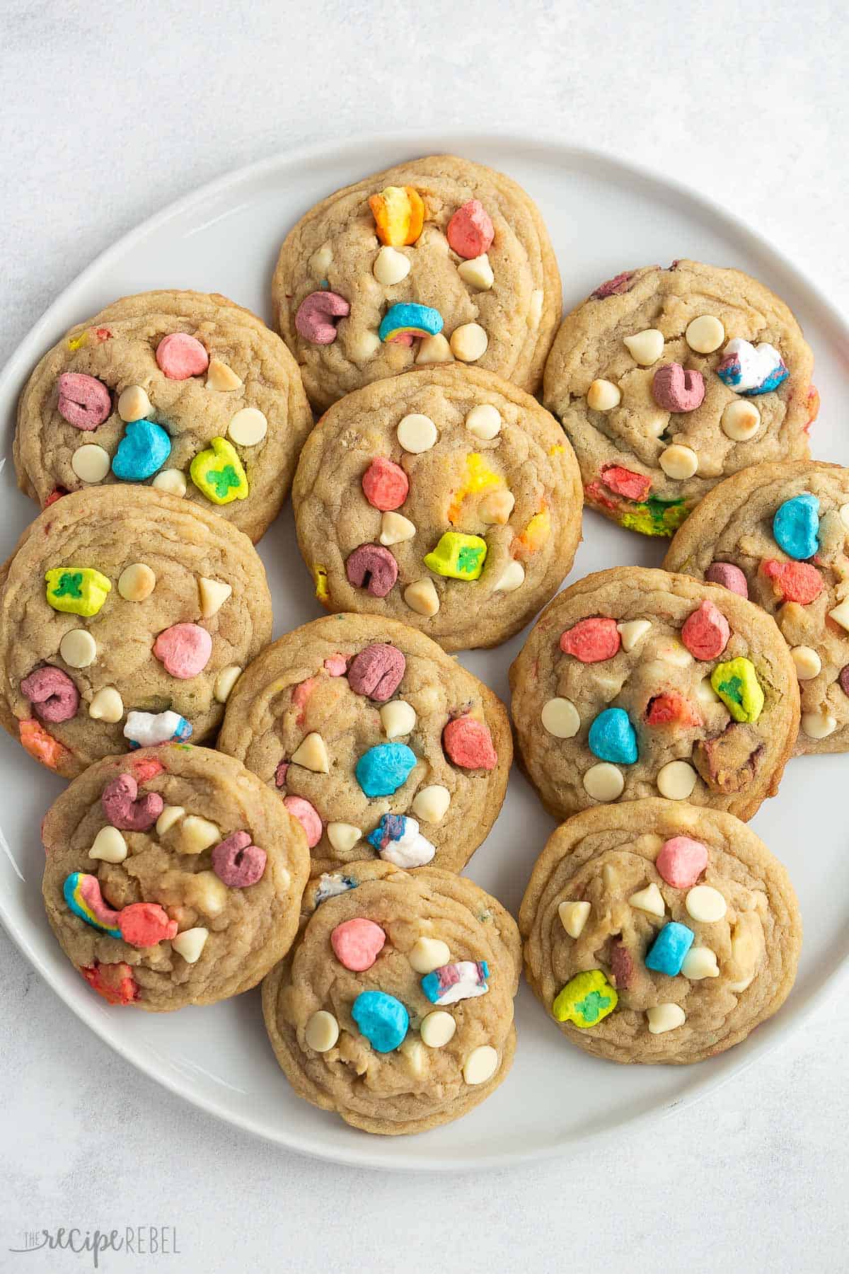 These White Chocolate Lucky Charms Cookies are perfectly chewy and made with Lucky Charms cereal and marshmallows. Perfect for St. Patrick's Day! Includes step by step recipe video. #cookies #recipe #dessert | st patrick's day | st. paddy's day | rainbow | cereal | cereal cookies | baking from scratch | cookie recipes overhead image of white chocolate lucky charms cookies on a white plate.