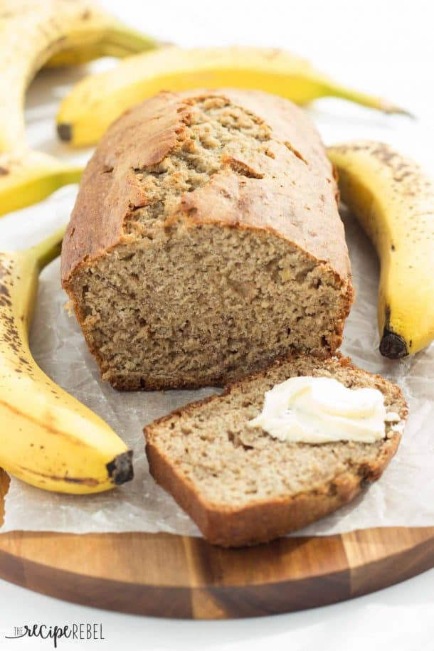 banana bread on cutting board with one banana on each side and butter on slice