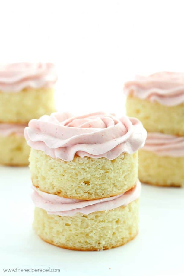 Mini Vanilla Layer Cakes with Strawberry Swiss Meringue Buttercream: the perfect moist vanilla cake and fluffy not-too-sweet strawberry frosting! Great for any birthday or Spring celebration. www.thereciperebel.com two layer mini vanilla cakes with pink frosting swirls on a white background