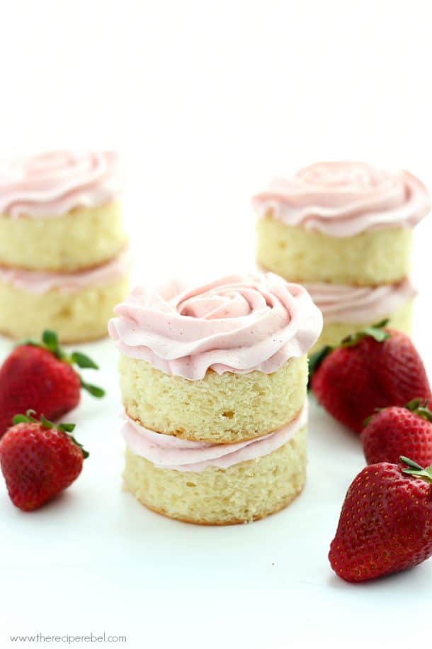 mini vanilla layer cakes with strawberry frosting and fresh strawberries on the side