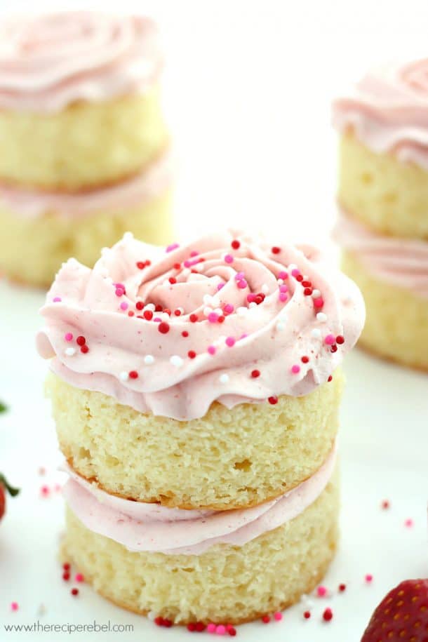 close up image of mini vanilla layer cake with strawberry frosting and pink and red sprinkles