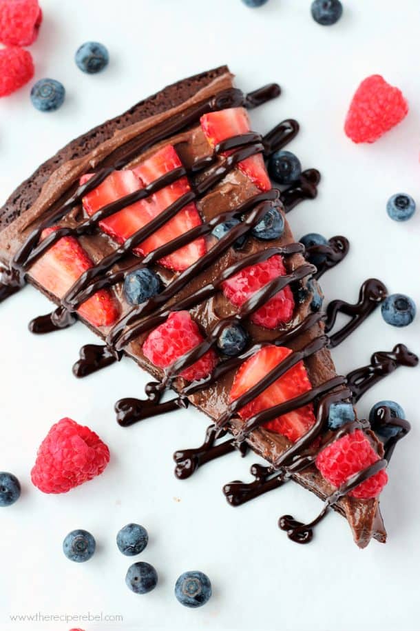 slice of nutella brownie fruit pizza on white background with chocolate drizzle on top