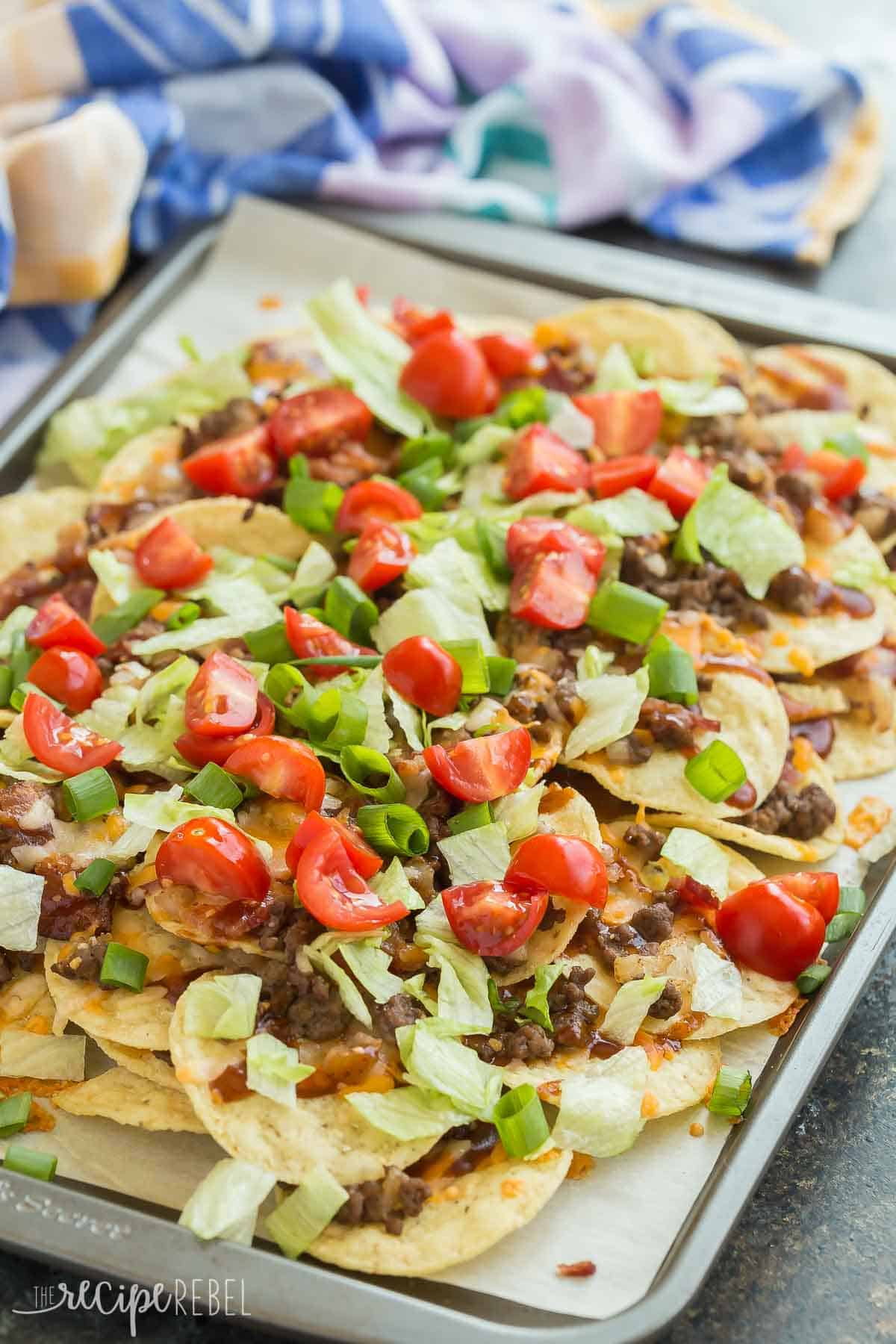 bbq bacon cheeseburger nachos close up on sheet pan with tomatoes lettuce and green onions