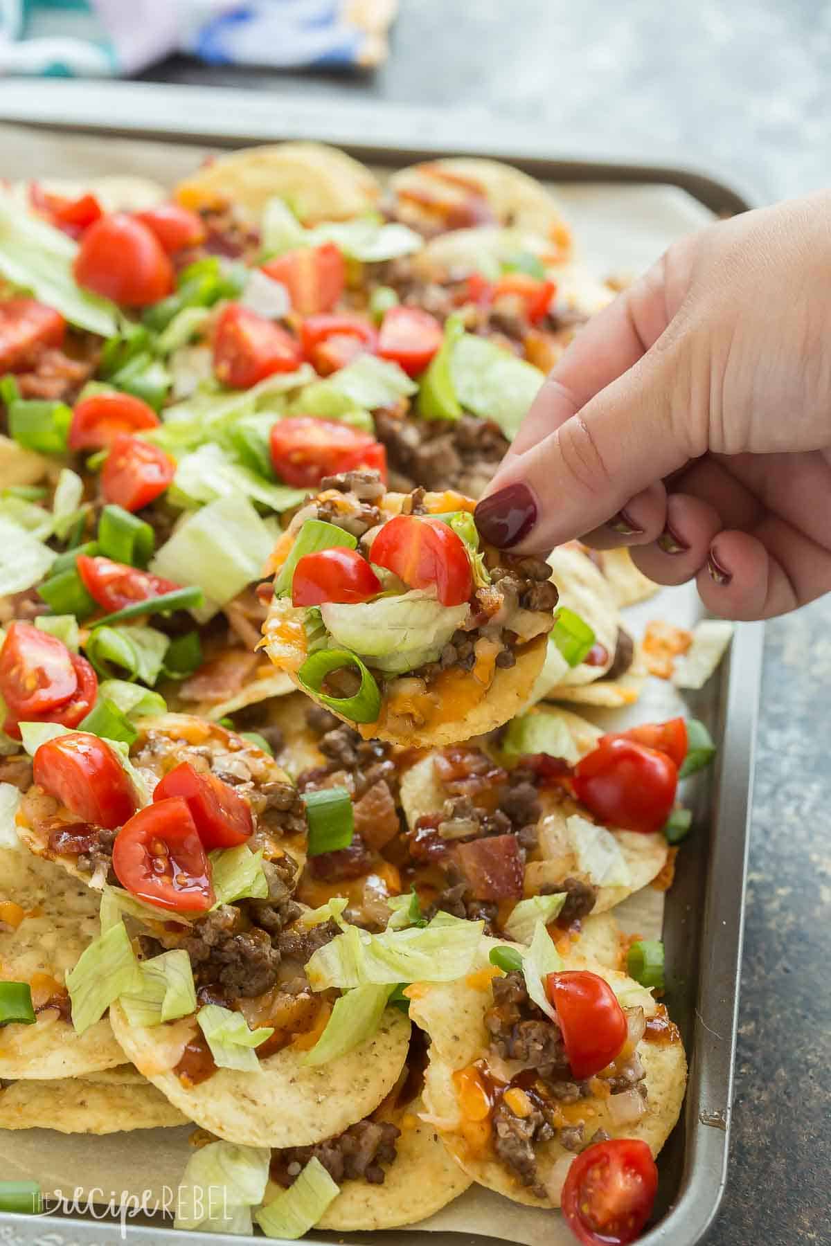 hand grabbing a bacon cheeseburger nacho from pan close up