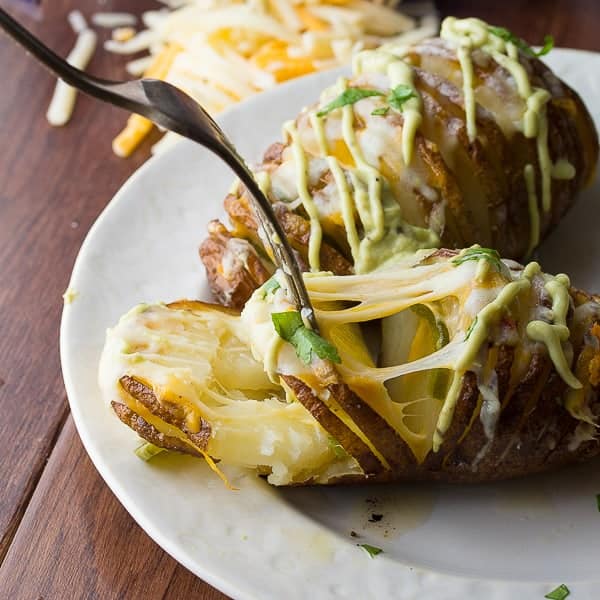 cheesy jalapeno hasselback potatoes on white plate with fork pulling potato apart