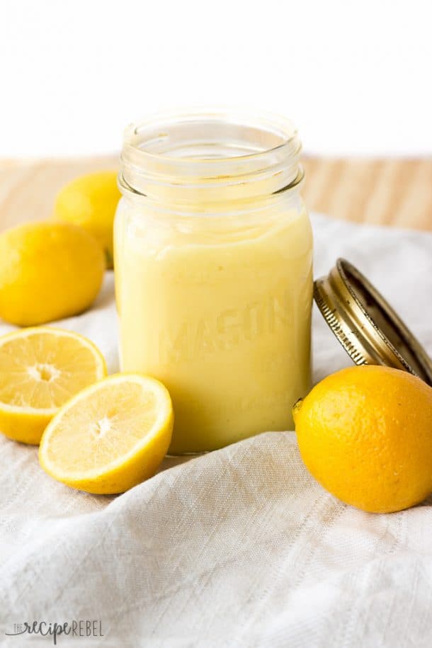 lemon curd in glass mason jar on grey towel with lemons around