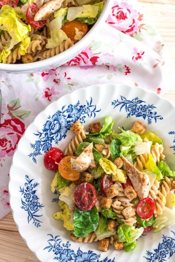 lighter chicken caesar pasta salad on white and blue plate with croutons
