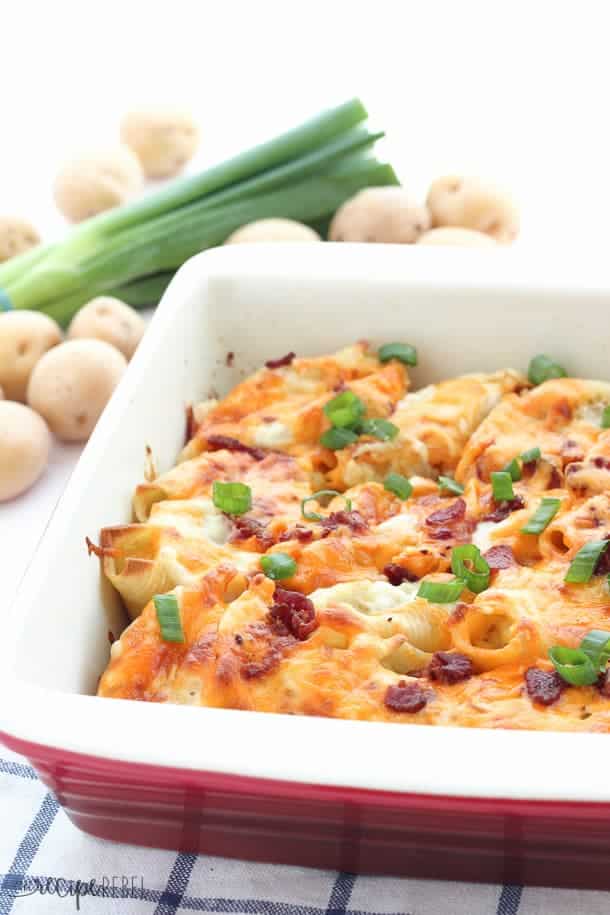 perogy stuffed shells in baking dish topped with bacon and green onions with potatoes in the background