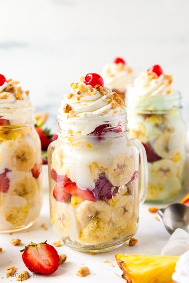 These Banana Split Trifles are made with white cake, vanilla pudding, bananas, strawberries and pineapple. Topped with whipped cream, nuts and a cherry, they are the perfect summer treat! #trifle #dessert | easy dessert | mason jar dessert | mini dessert | cake mix recipe banana split trifle in mason jar with whipped cream