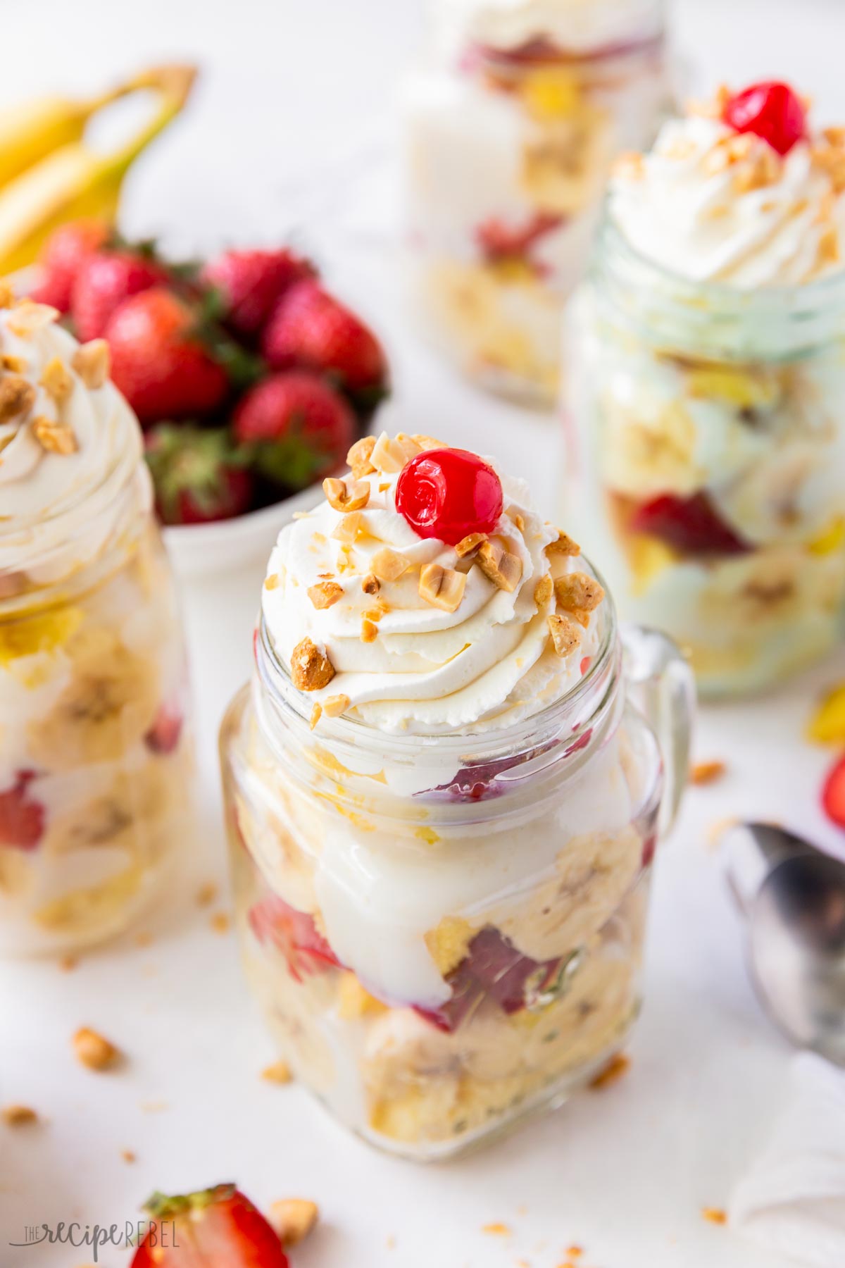 These Banana Split Trifles are made with white cake, vanilla pudding, bananas, strawberries and pineapple. Topped with whipped cream, nuts and a cherry, they are the perfect summer treat! #trifle #dessert | easy dessert | mason jar dessert | mini dessert | cake mix recipe close up of banana split trifle with whipped cream