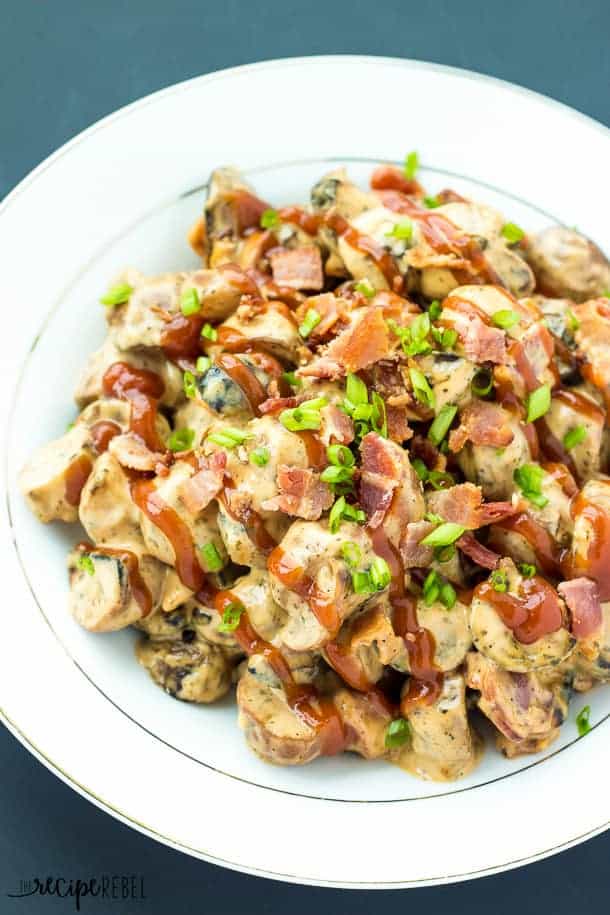 bbq bacon potato salad on white plate with drizzle of barbecue sauce and topped with green onions