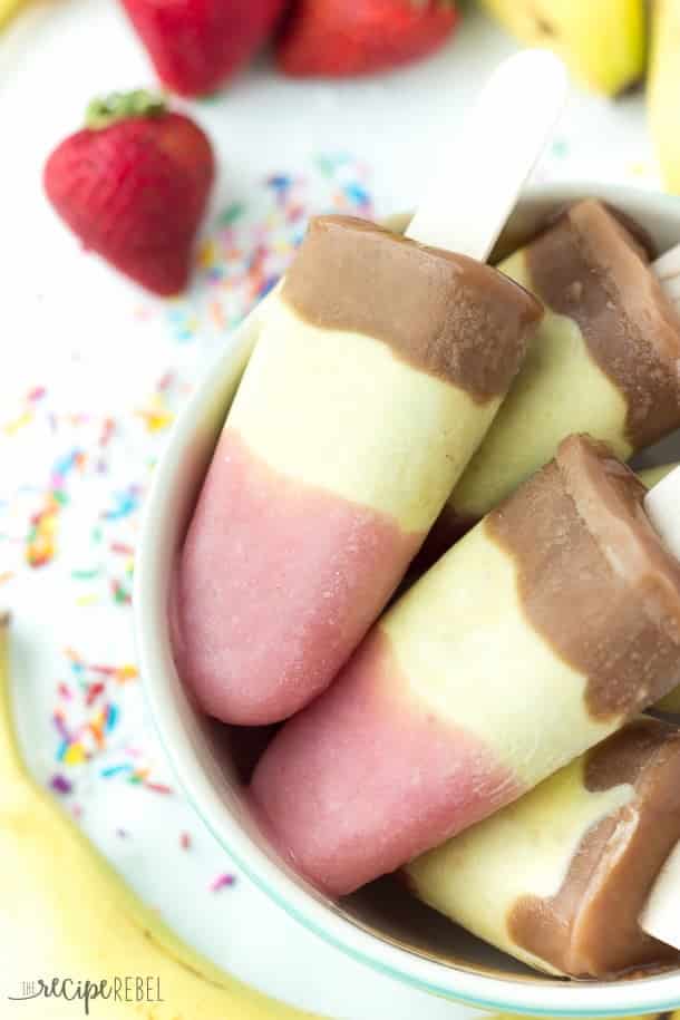 Banana Split Pudding Popsicles: 3 layers of creamy, frozen pudding: strawberry, banana pineapple and chocolate! The easy way to enjoy a banana split this summer! www.thereciperebel.com three layer banana split pudding pops with pink white and chocolate brown layers on wooden popsicle sticks