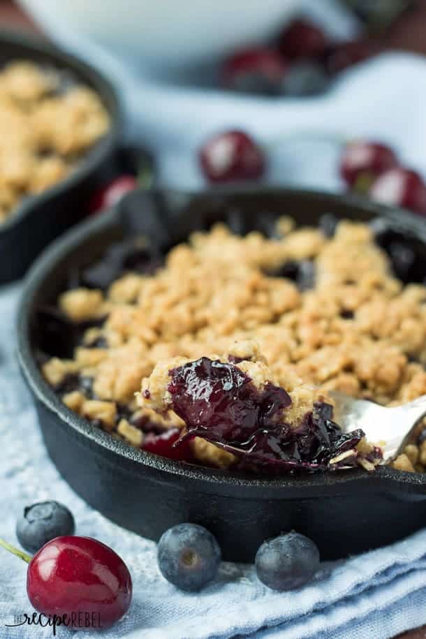 close up image of spoon scooping berry cherry crisp from individual cast iron skillet