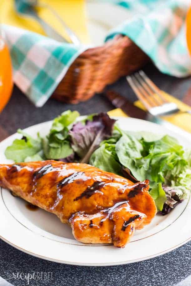 white plate with chicken breast and greens in front of basket with blue napkin