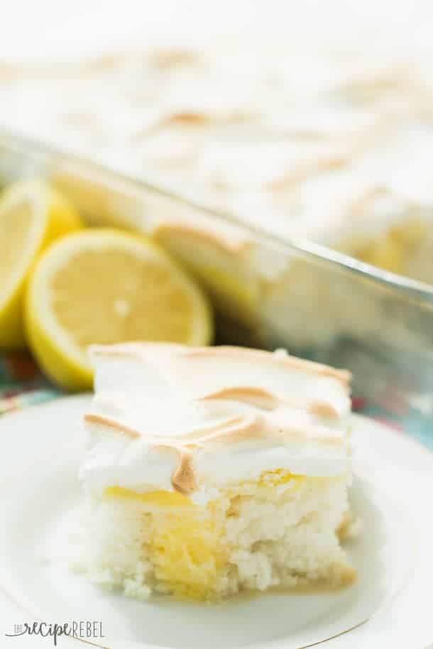 one piece of skinny lemon meringue poke cake on white plate with lemons behind