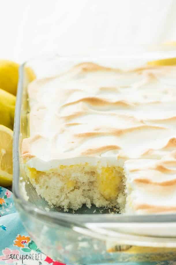 glass pan with lemon meringue poke cake with one piece missing revealing lemon curd filling