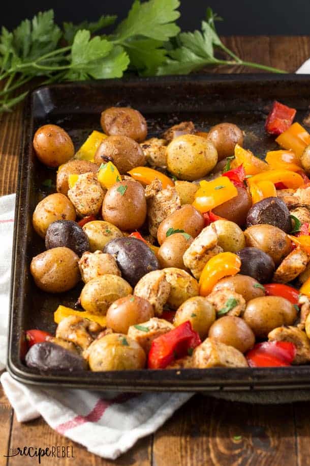 dark sheet pan with chunks of chicken peppers and baby potatoes with parsley in the background