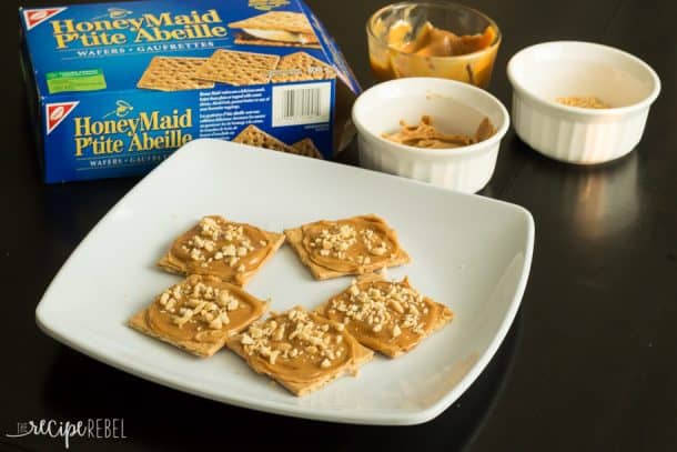 graham crackers on plate spread with peanut butter caramel sauce and sprinkled with chopped peanuts