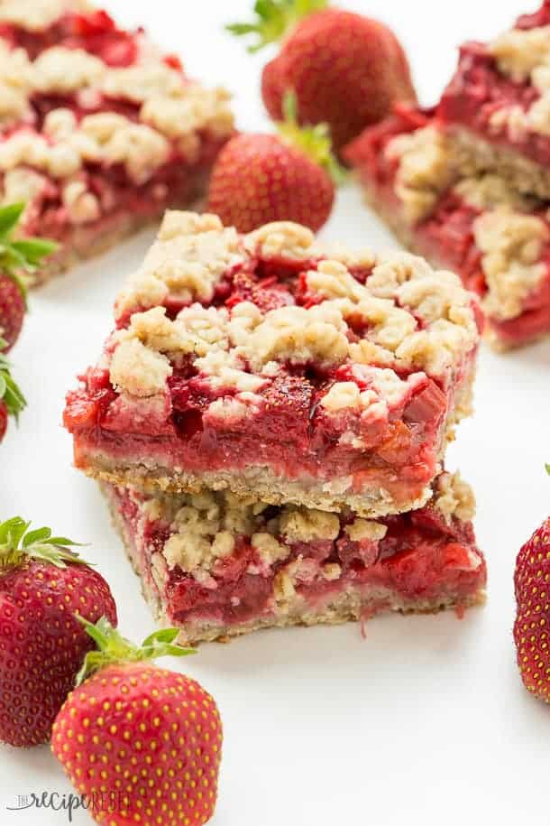 two strawberry rhubarb crisp bars stacked with fresh strawberries all around