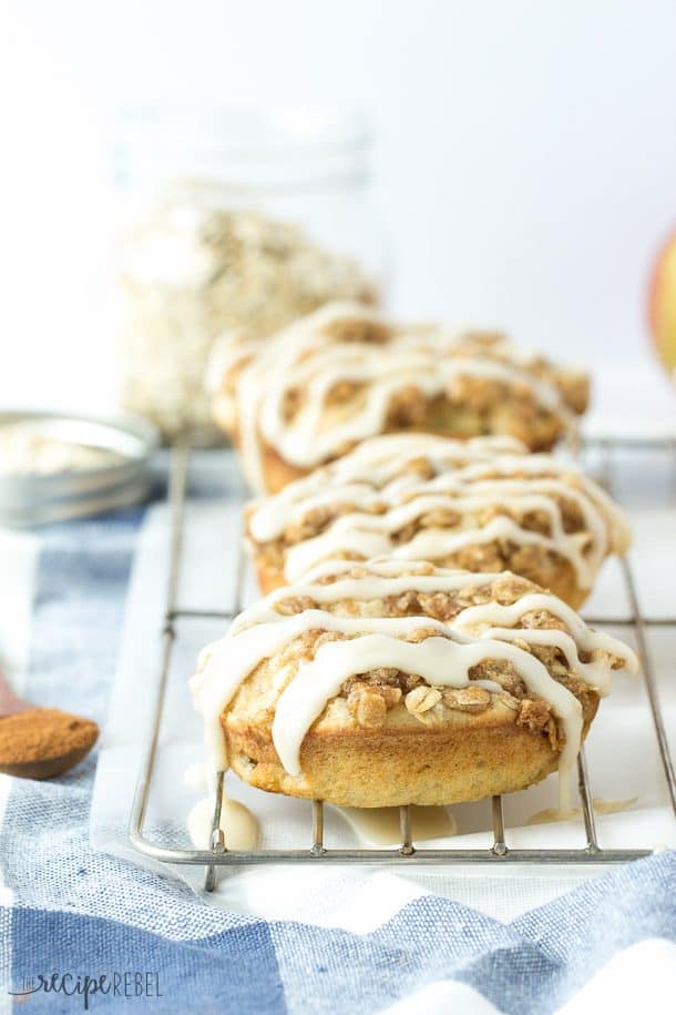 a row of apple crisp donuts on a wire cooling rack over a white and blue towel