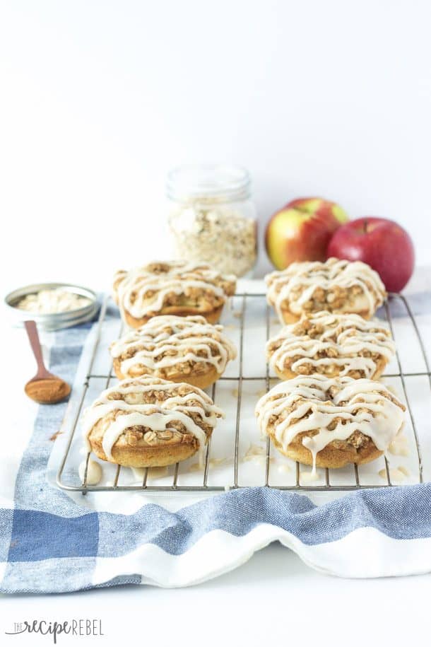 six maple glazed apple crisp donuts on cooling rack with apples and oats in the background