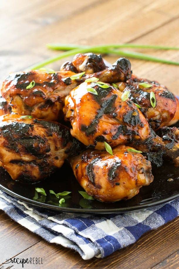 black plate piled with grilled chicken drumsticks on a wooden background