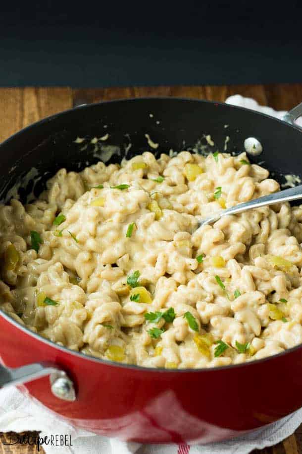 green chile mac and cheese in black and red pot with metal serving spoon stuck in pasta