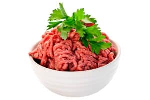 image of a white bowl filled with raw ground beef and parsley on top