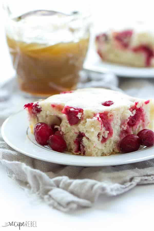 vanilla cake with lots of cranberries on a white plate with caramel sauce in the background 