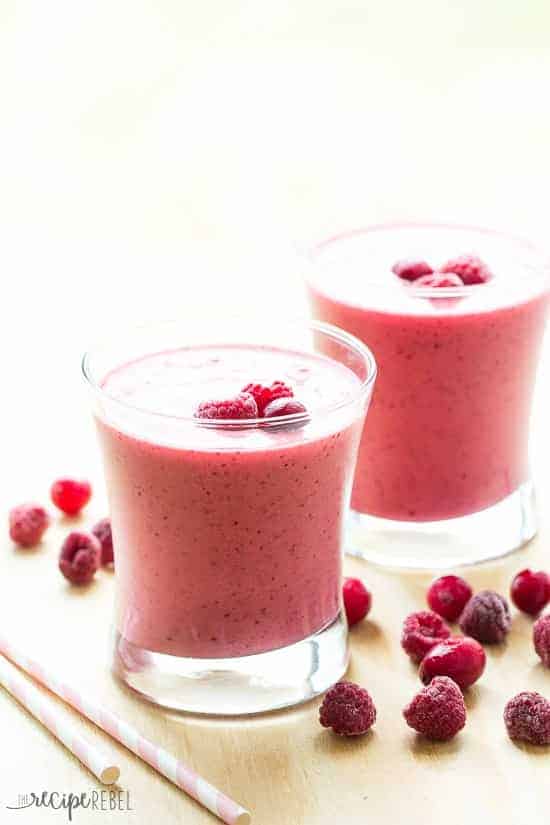 two short glasses with cranberry raspberry smoothie and frozen cranberries and raspberries all around