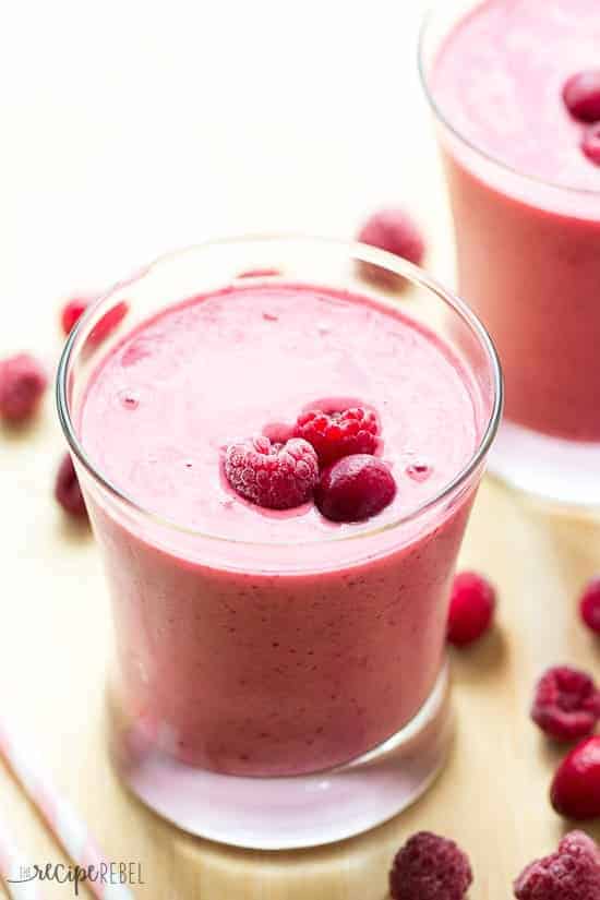 close up image of cranberry raspberry smoothie in short glass with raspberries and cranberry on top