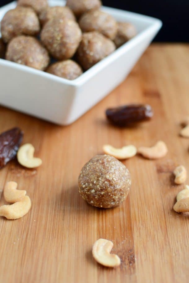 3 ingredient cashew date snack balls on wooden cutting board with cashews and dates in the background