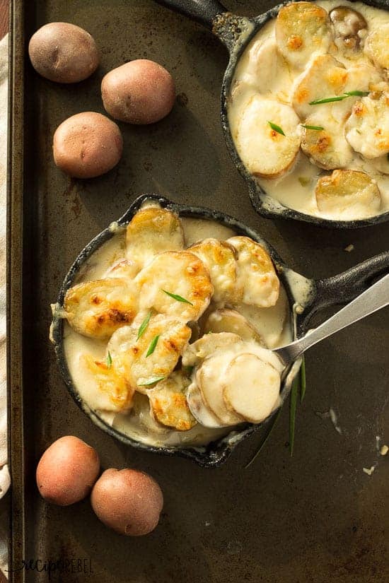 overhead image of two small skillets of scalloped potatoes and a spoon scooping some potatoes