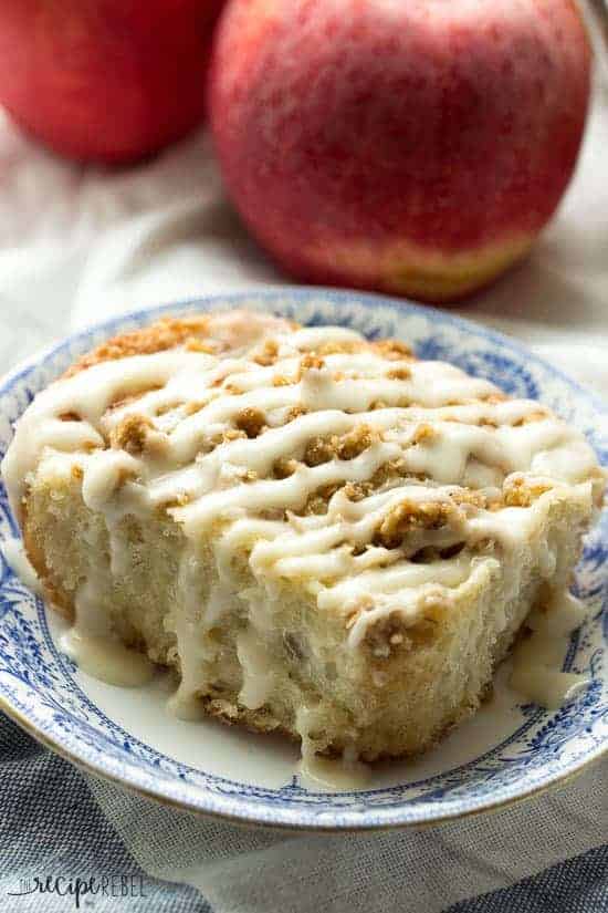 one apple crisp cinnamon bun on white and blue plate with whole apples behnid