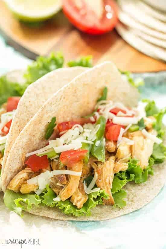 close up image of slow cooker honey sriracha chicken tacos on soft tortillas with lettuce tomatoes and cheese