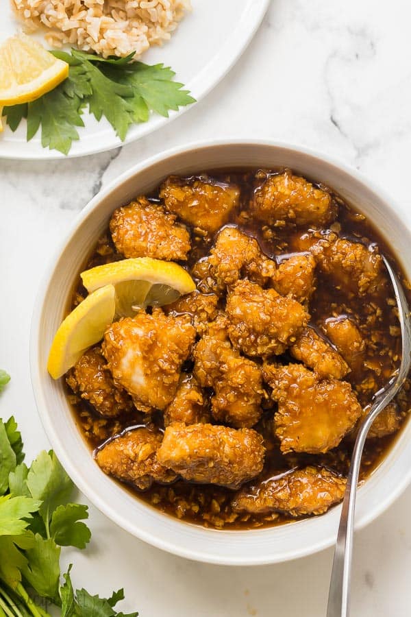 honey lemon chicken in white bowl overhead with spoon and lemon wedges in bowl