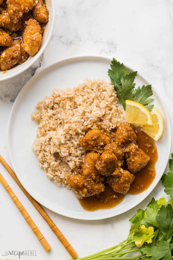 honey lemon chicken and rice on white plate overhead with lemon wedges and chopsticks