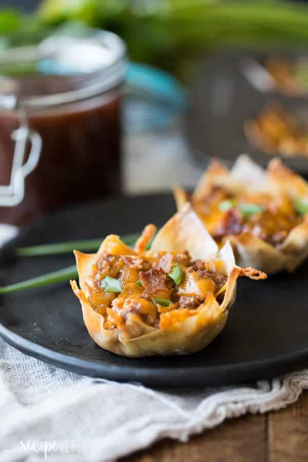 bacon cheeseburger cupcakes in wonton wrappers on black plate topped with green onions