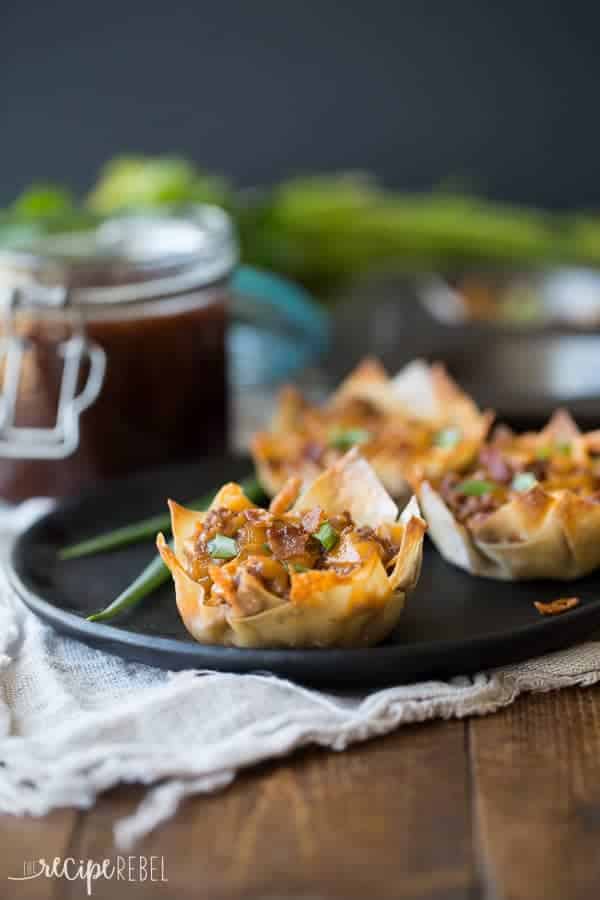 Bacon, beef, barbecue sauce and cheese stuffed into a wonton wrapper and baked until crispy -- the perfect finger food for game day or any party! bbq bacon cheeseburger cupcakes on a black plate on a wooden background