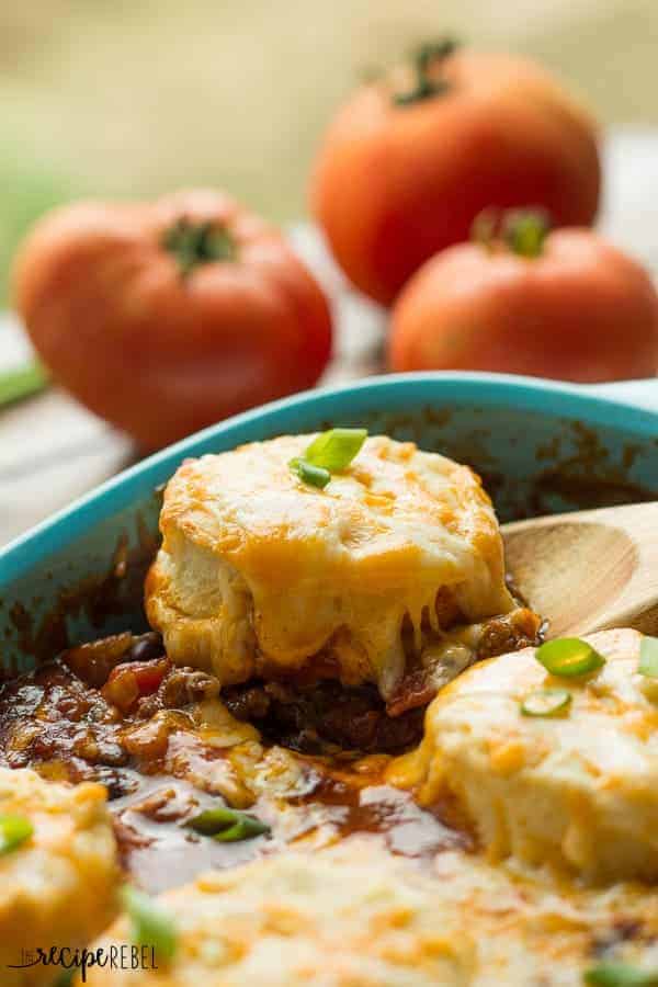 close up image of biscuit with cheese on top being scooped out of pan with chili