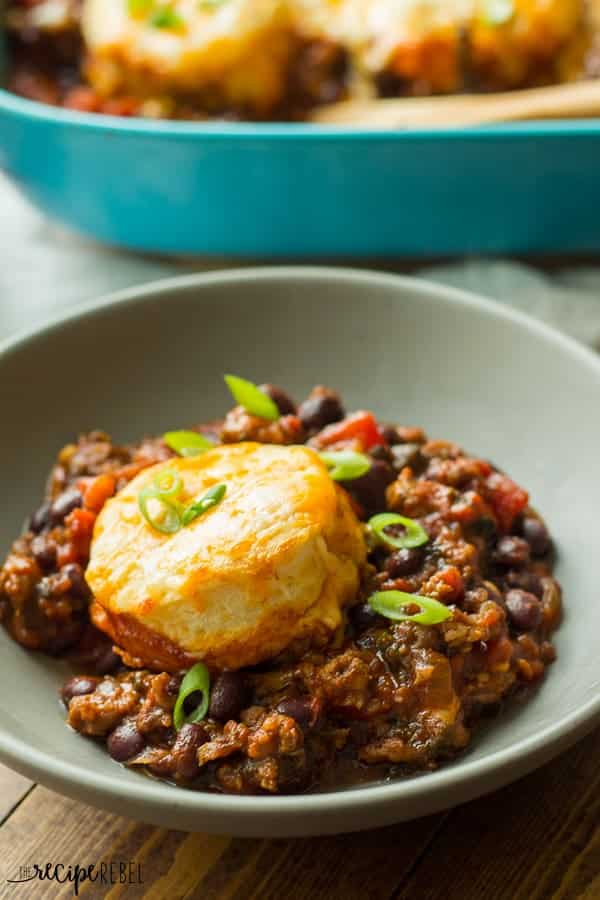 a grey bowl with chili and topped with a cheesy biscuit and green onions