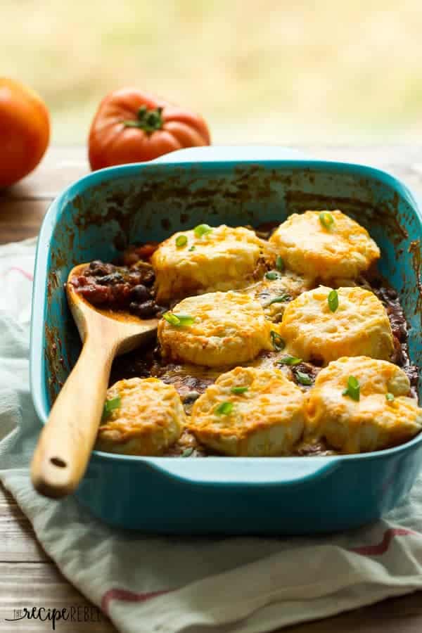 bbq chili cheese biscuit casserole in blue baking dish with wooden spoon stuck in and fresh tomatoes in the background