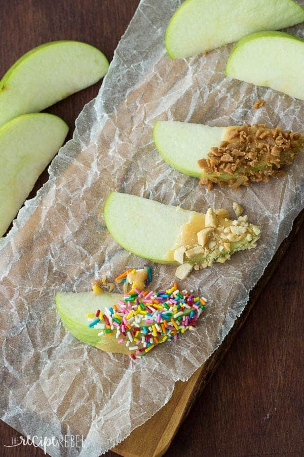 three apple slices dipped in caramel dip and covered in sprinkles toffee bits or peanuts