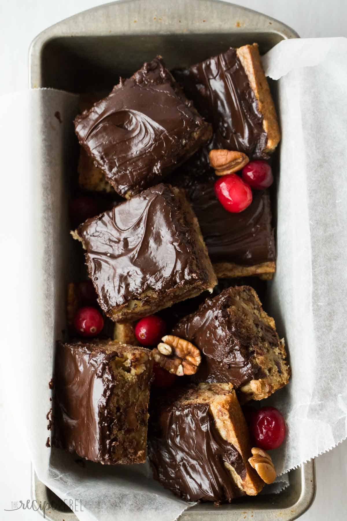 squares of chocolate cranberry blondies stacked in tin loaf pan with parchment paper
