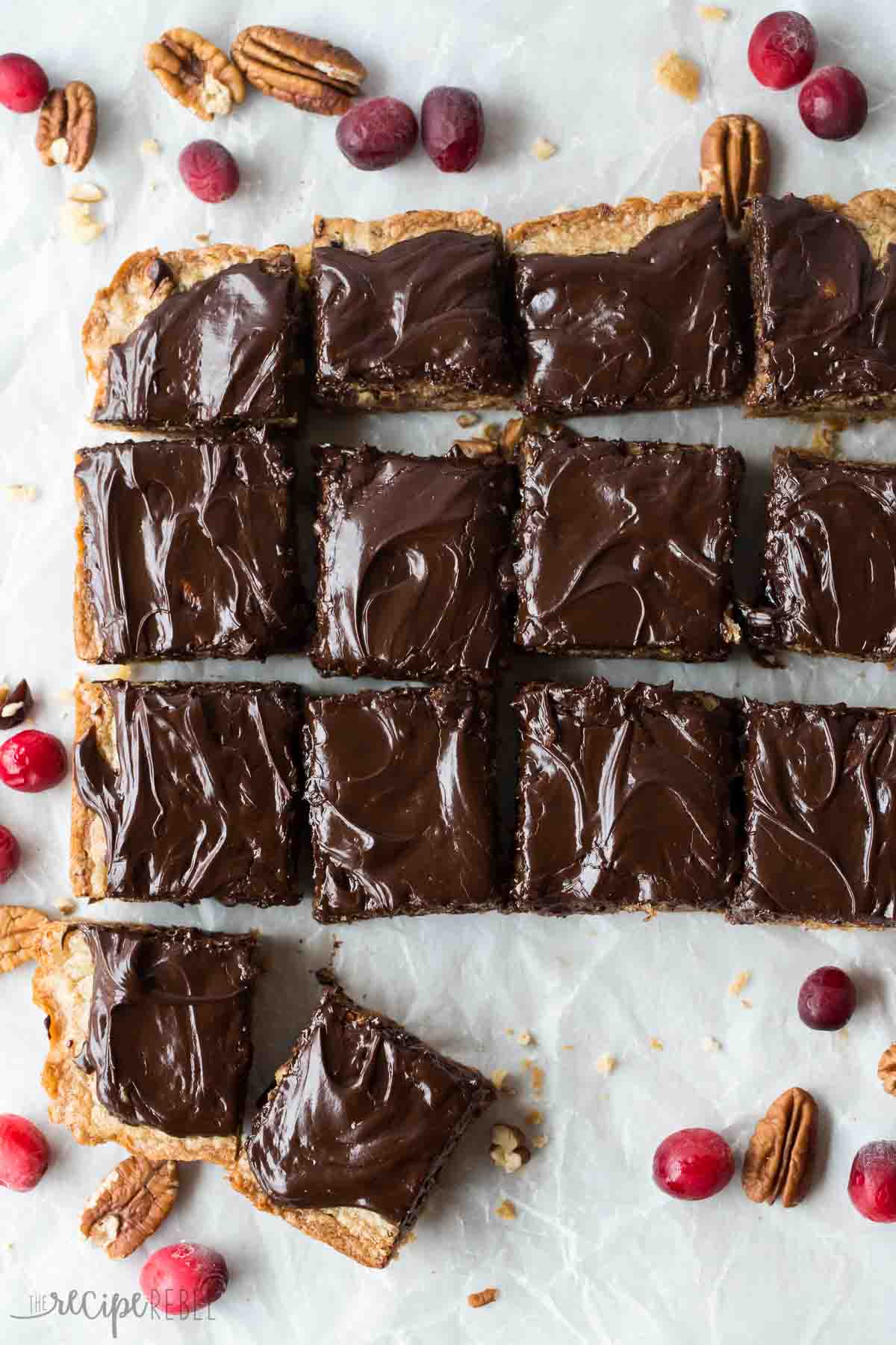 dark chocolate cranberry blondies cut into squares on parchment paper with pecans and cranberries all around